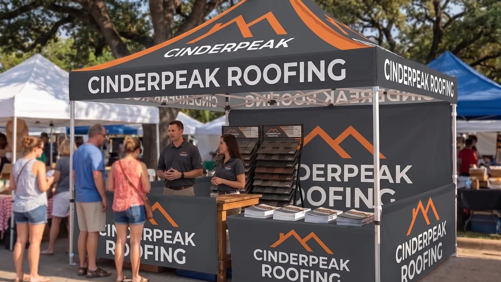 A dark gray and orange custom 10 x 10 canopy for a fictional roofing company, with printed walls, set up among other tents at an outdoor market