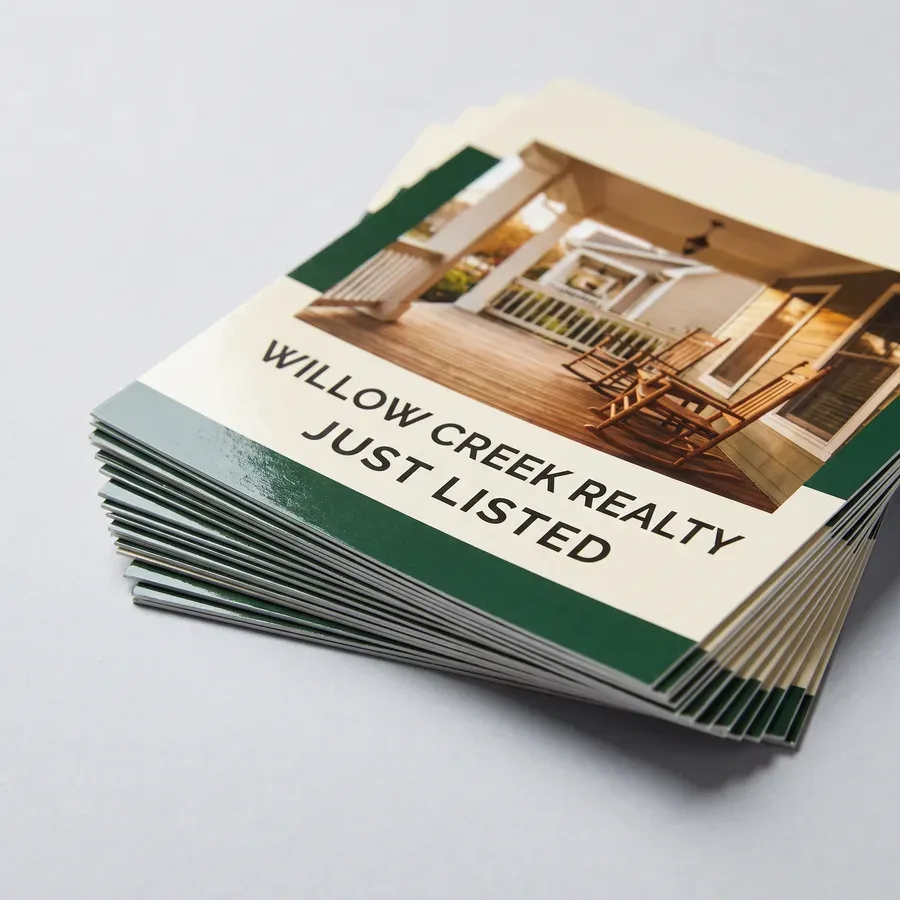 A stack of full color 4 x 6 inch Willow Creek Realty just listed postcards on thick glossy 16pt cardstock on a pale gray surface