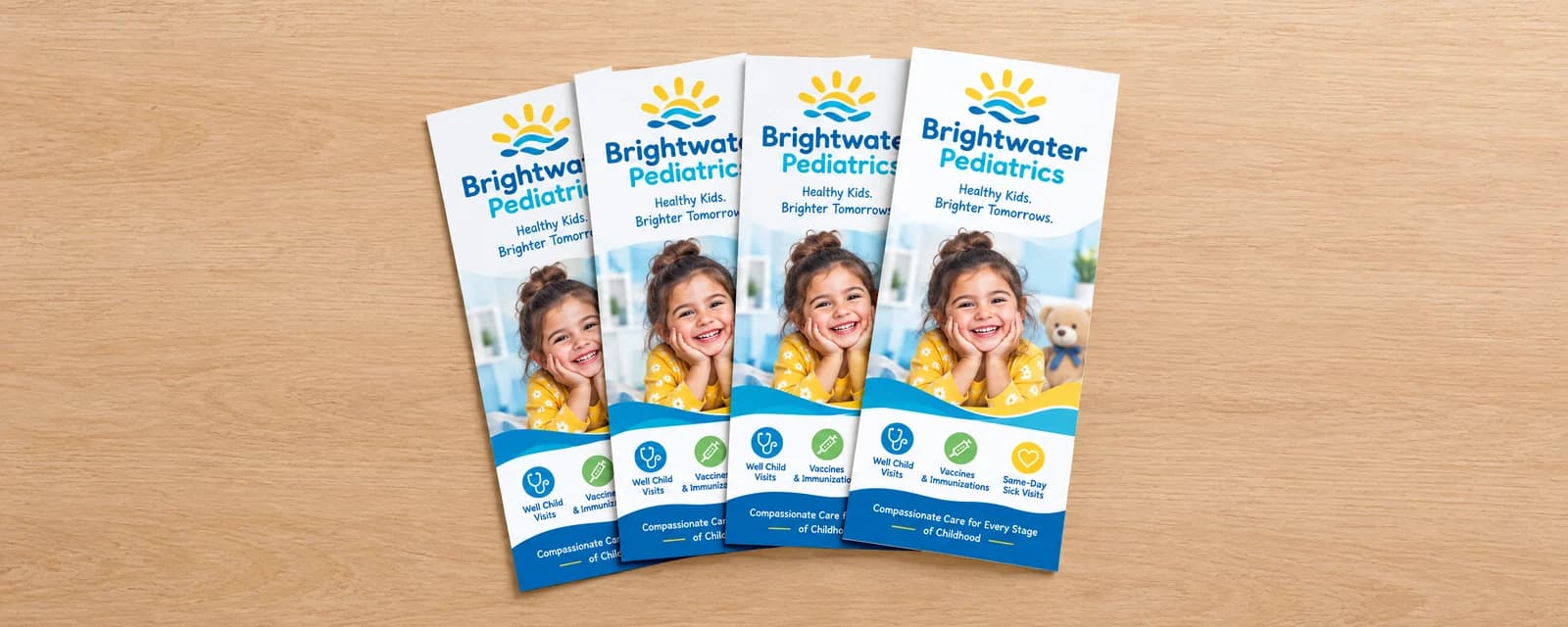 Four full-color pediatric clinic rack cards with a smiling child photo laid side by side on a light wood surface