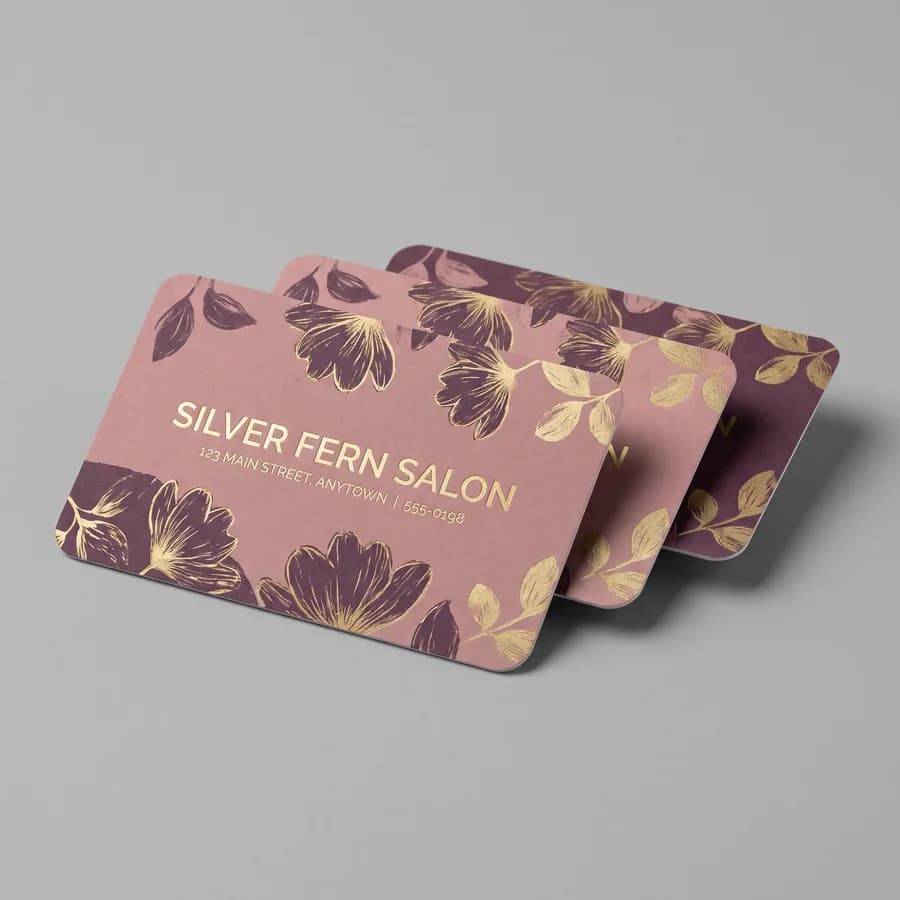 Dusty rose and gold rounded corner business cards for the fictional Silver Fern Salon fanned on a gray surface
