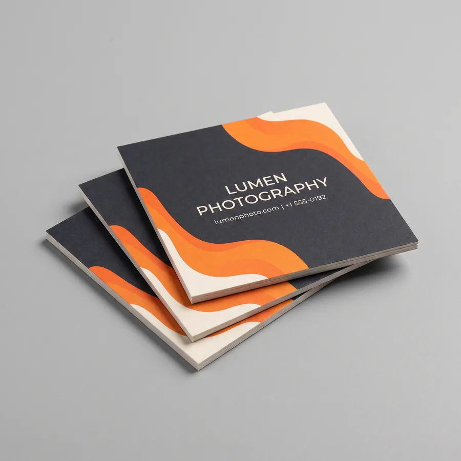 Charcoal and orange square business cards for the fictional Lumen Photography stacked on a gray surface