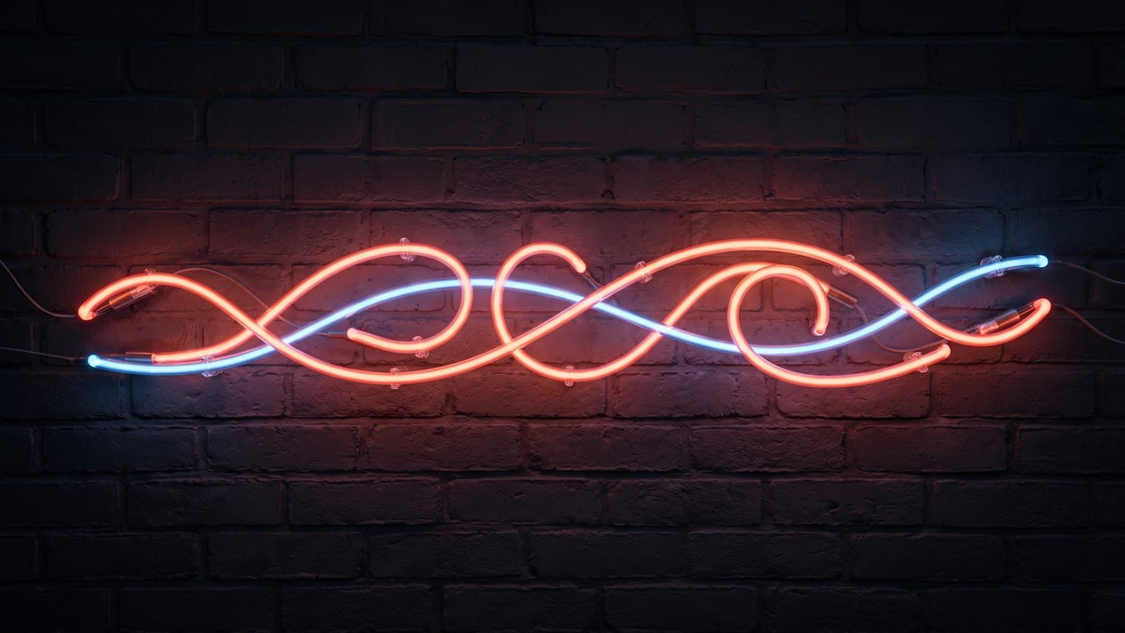 Hand bent glass neon tubing glowing red orange against a dark workshop wall, the sealed tube ends and electrode housings visible at the end of each run