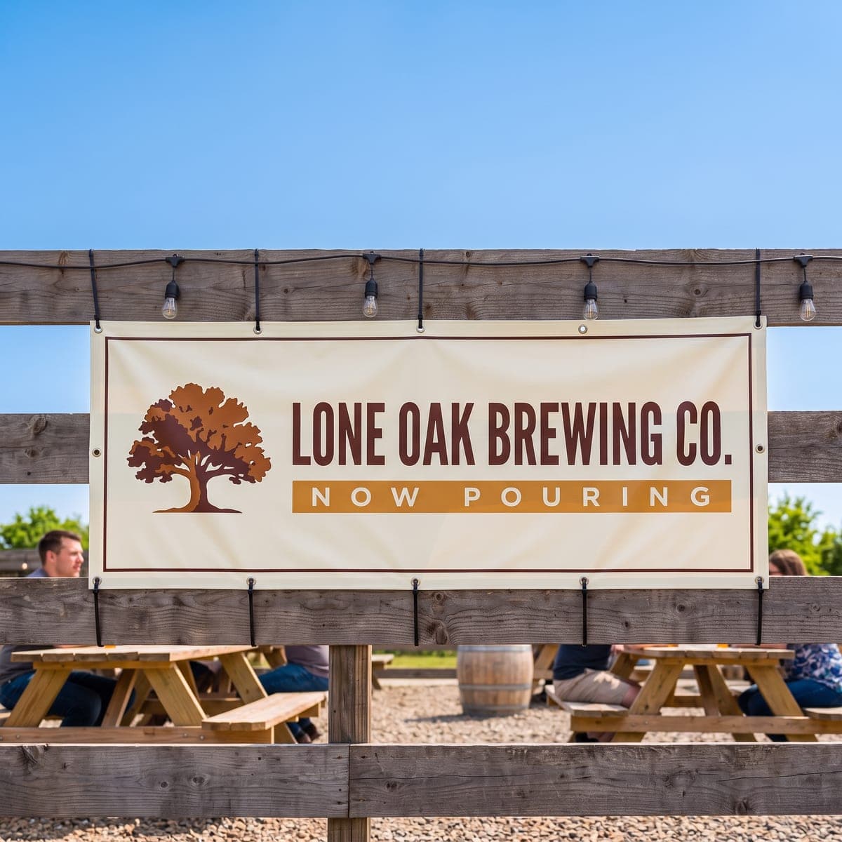 The finished Lone Oak Brewing Co. banner tied to a wooden fence above picnic tables in a sunny beer garden