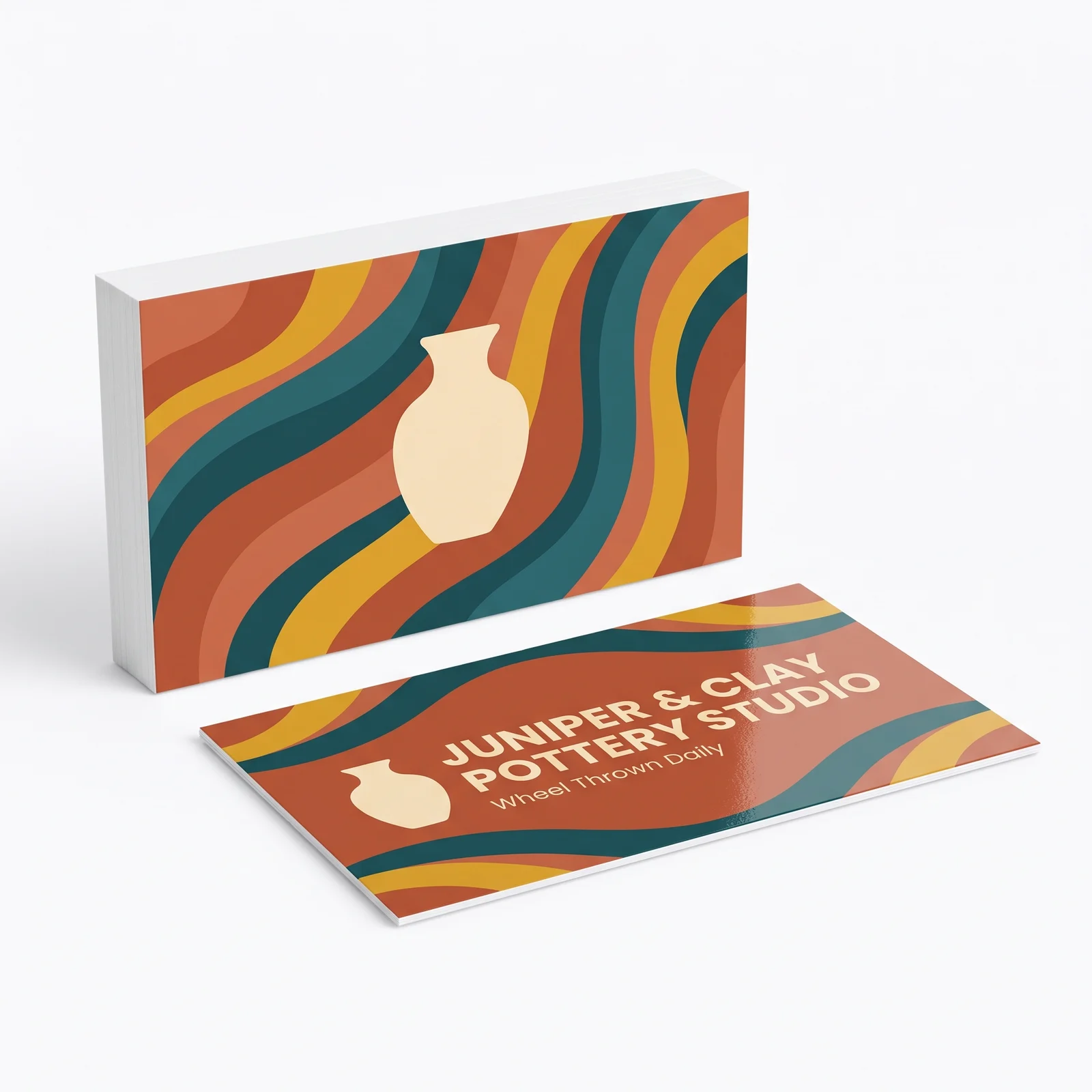 A standing stack of full color business cards for a pottery studio showing the patterned back, with one card lying face up in front of it showing the studio name and tagline