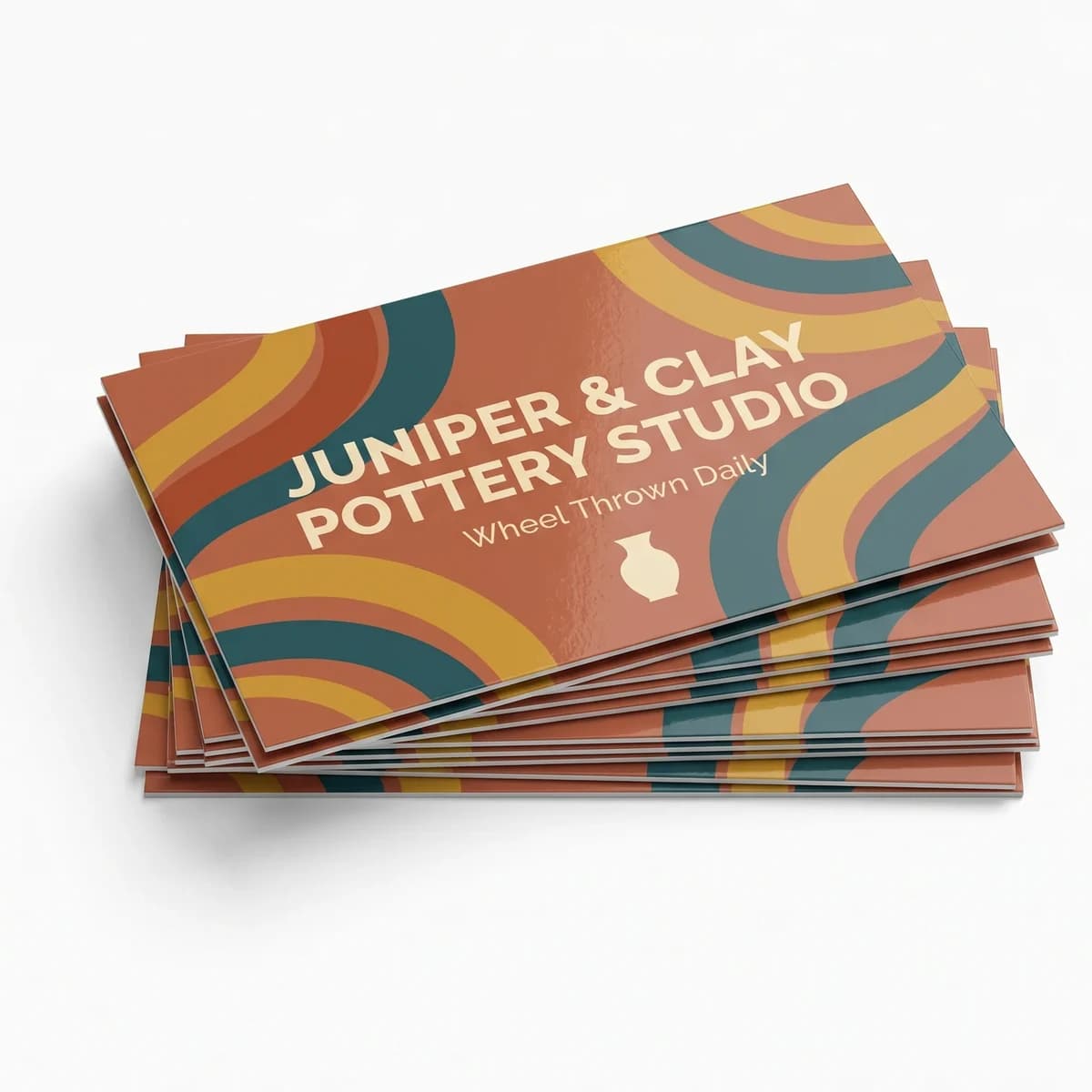 A fanned stack of full color terracotta, teal and mustard business cards for a fictional pottery studio on a white studio ground