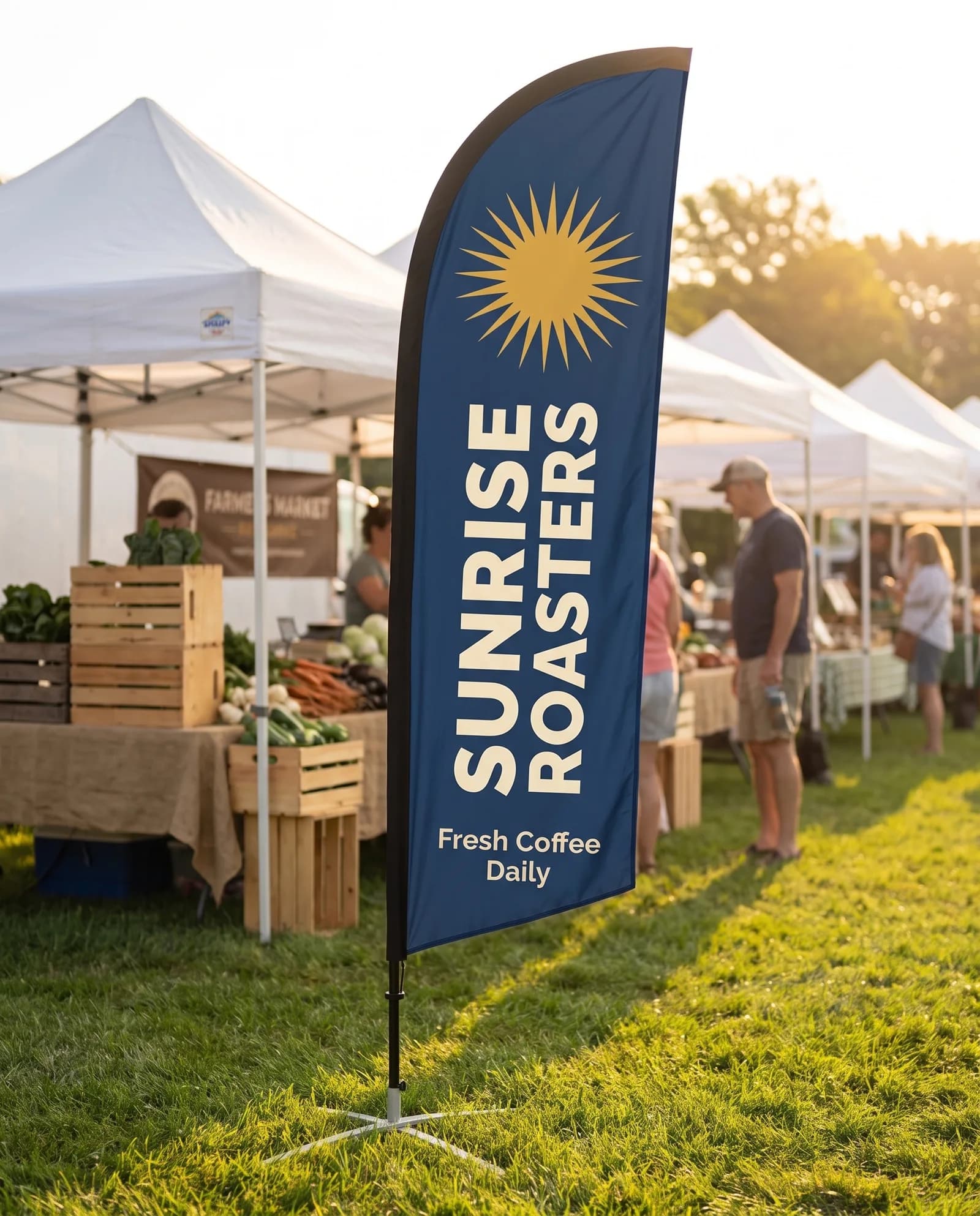 Navy Sunrise Roasters feather flag standing on the grass at an outdoor market with white canopy tents