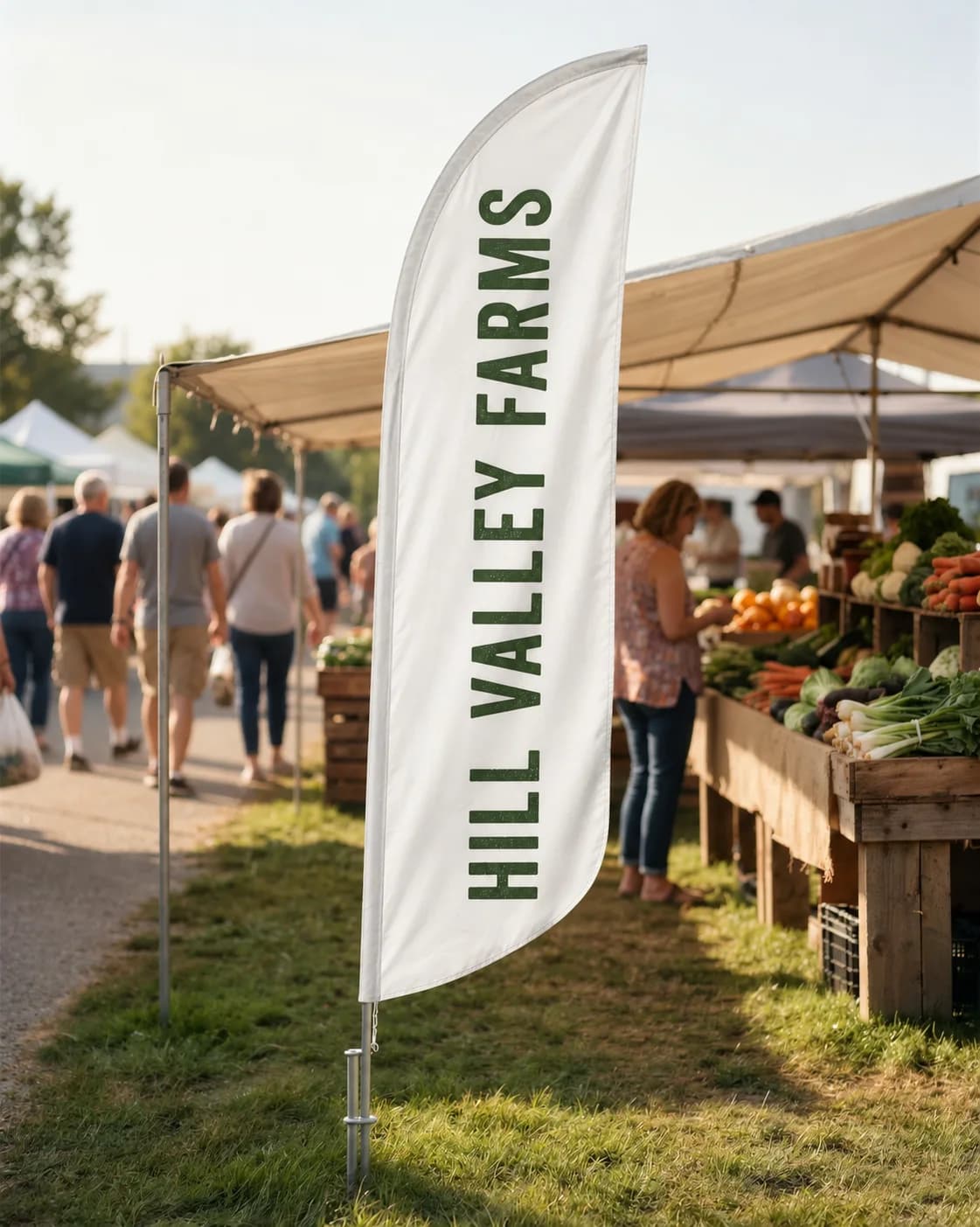 White convex feather flag with green vertical lettering on a ground spike in grass beside a produce stand