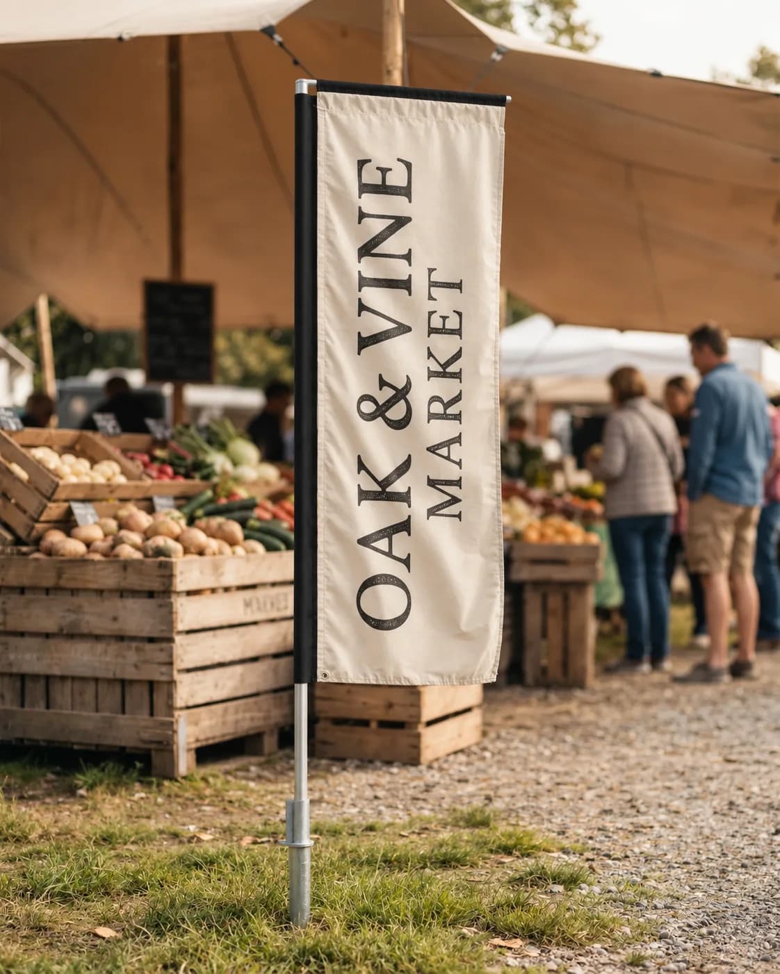 Cream rectangle flag with dark vertical lettering on a ground spike in grass beside produce crates under a canopy