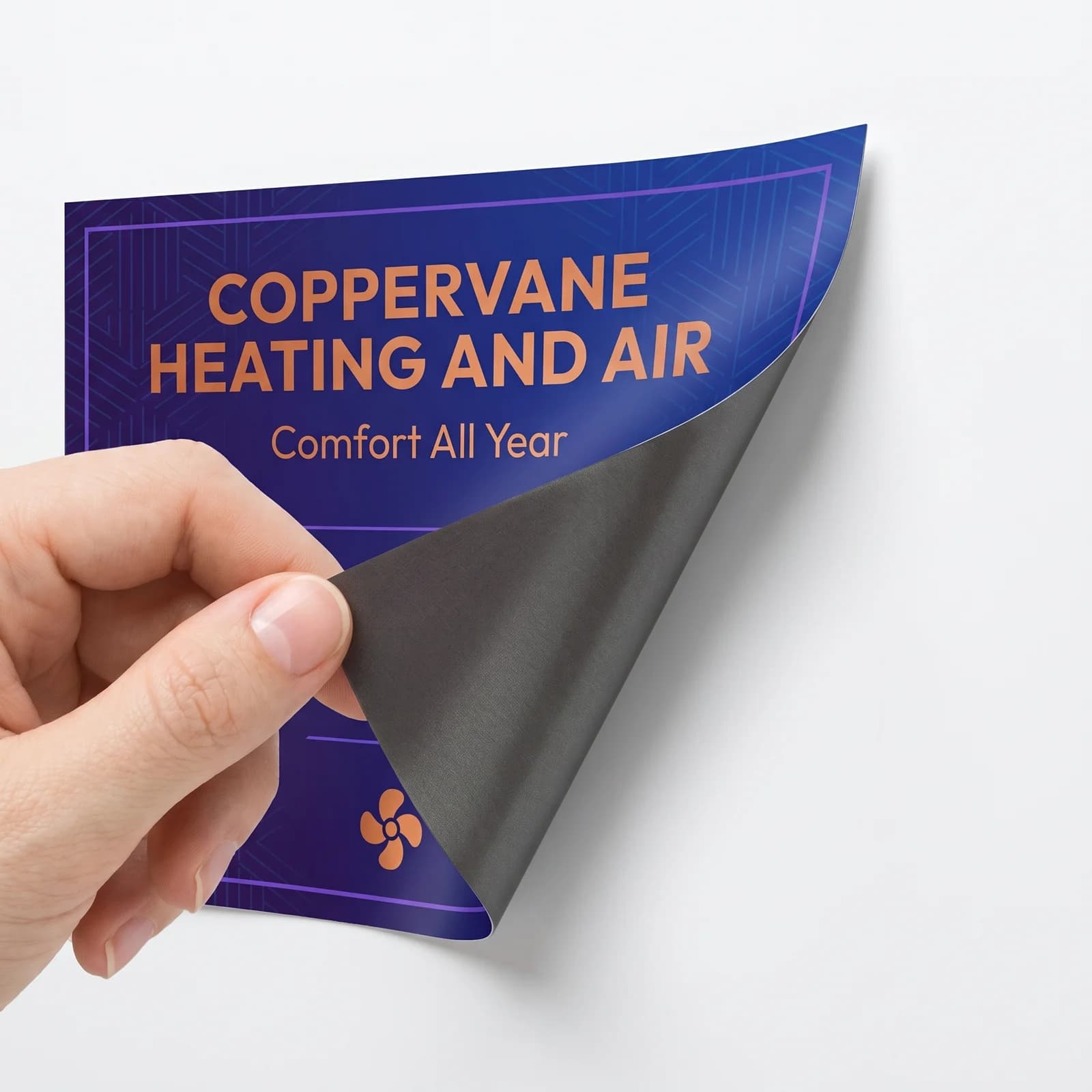 A hand peeling the corner of a Coppervane Heating and Air vehicle magnet, showing the dark magnetic backing