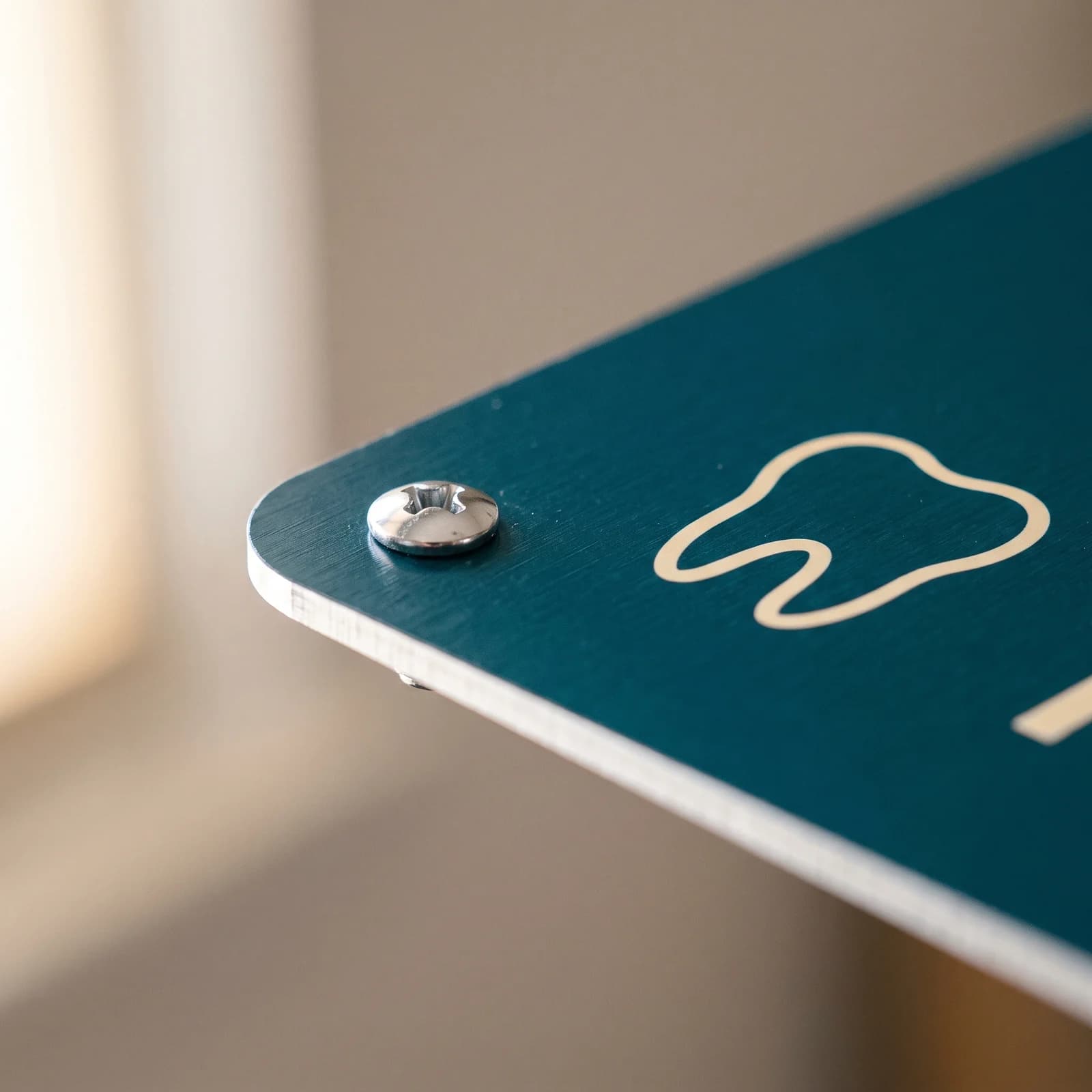 Close view of a screw head seated in a drilled hole at the corner of a teal aluminum sign