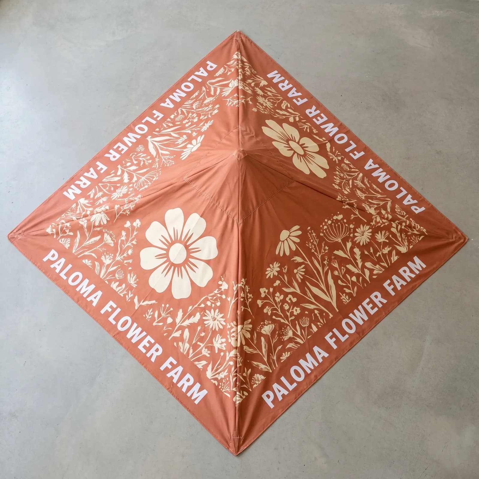 A dye-sublimated canopy top printed for a fictional flower farm, laid flat on a floor with no frame