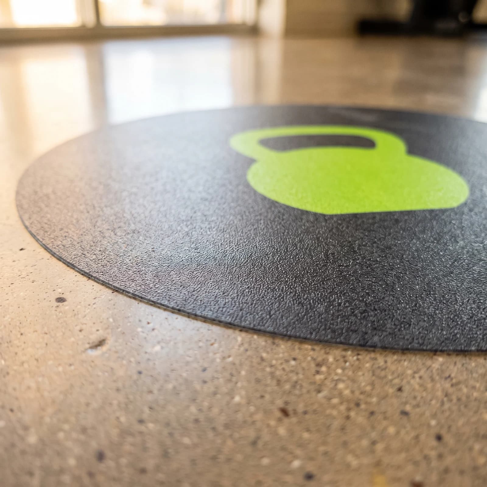 Close view of a textured black circular floor graphic with a green kettlebell on sealed concrete