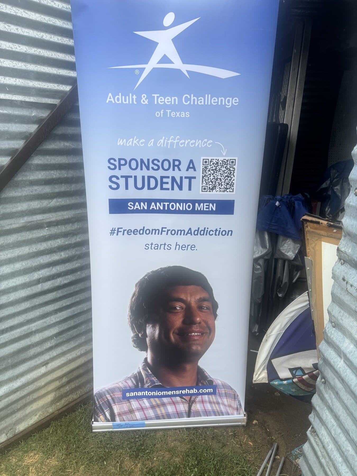On-site photo of the Adult and Teen Challenge banner set up outdoors beside the storage shed