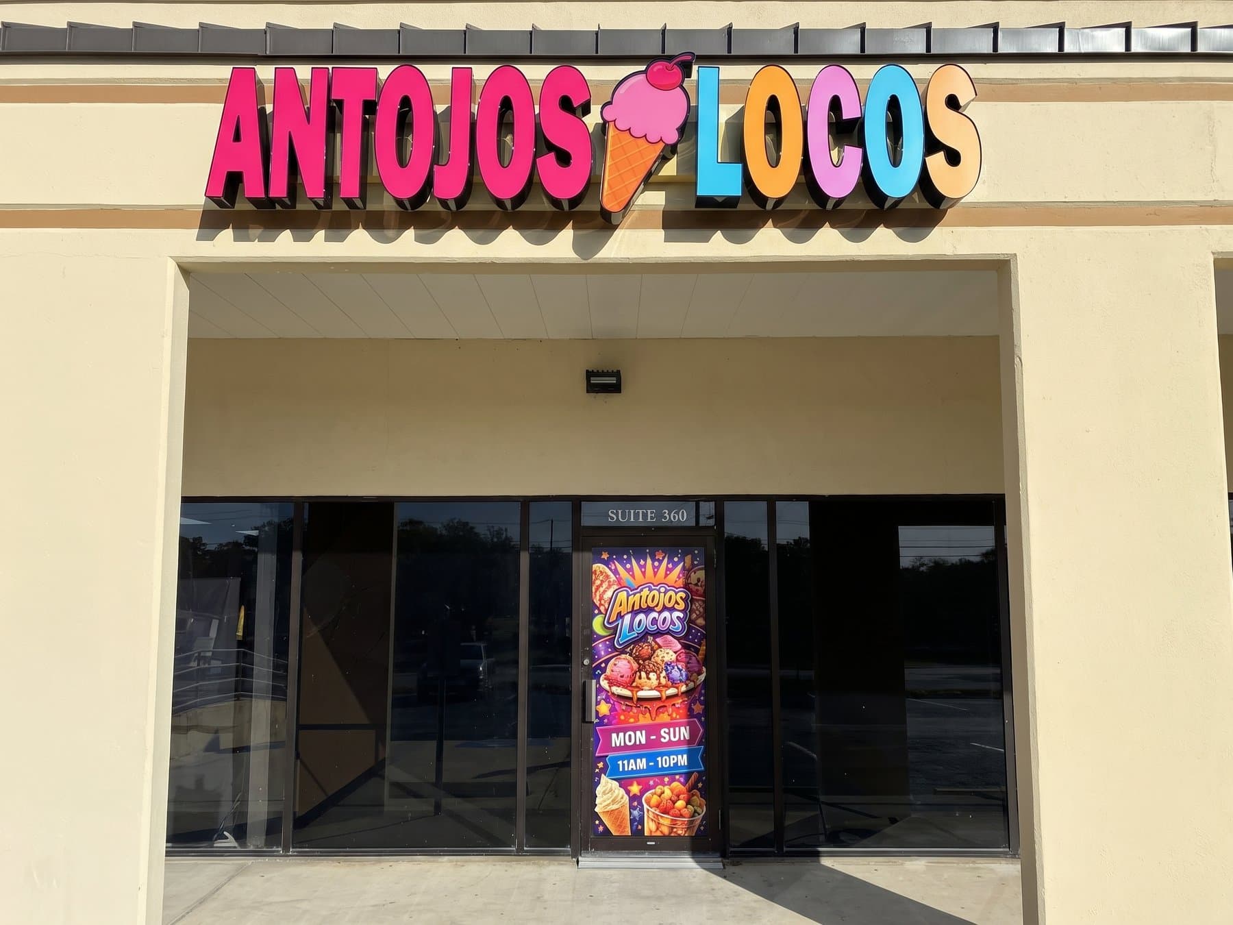 Antojos Locos dimensional letters in the brand colors across the stucco fascia above the entry, with the matching printed door graphic carrying the logo, food photography and daily hours