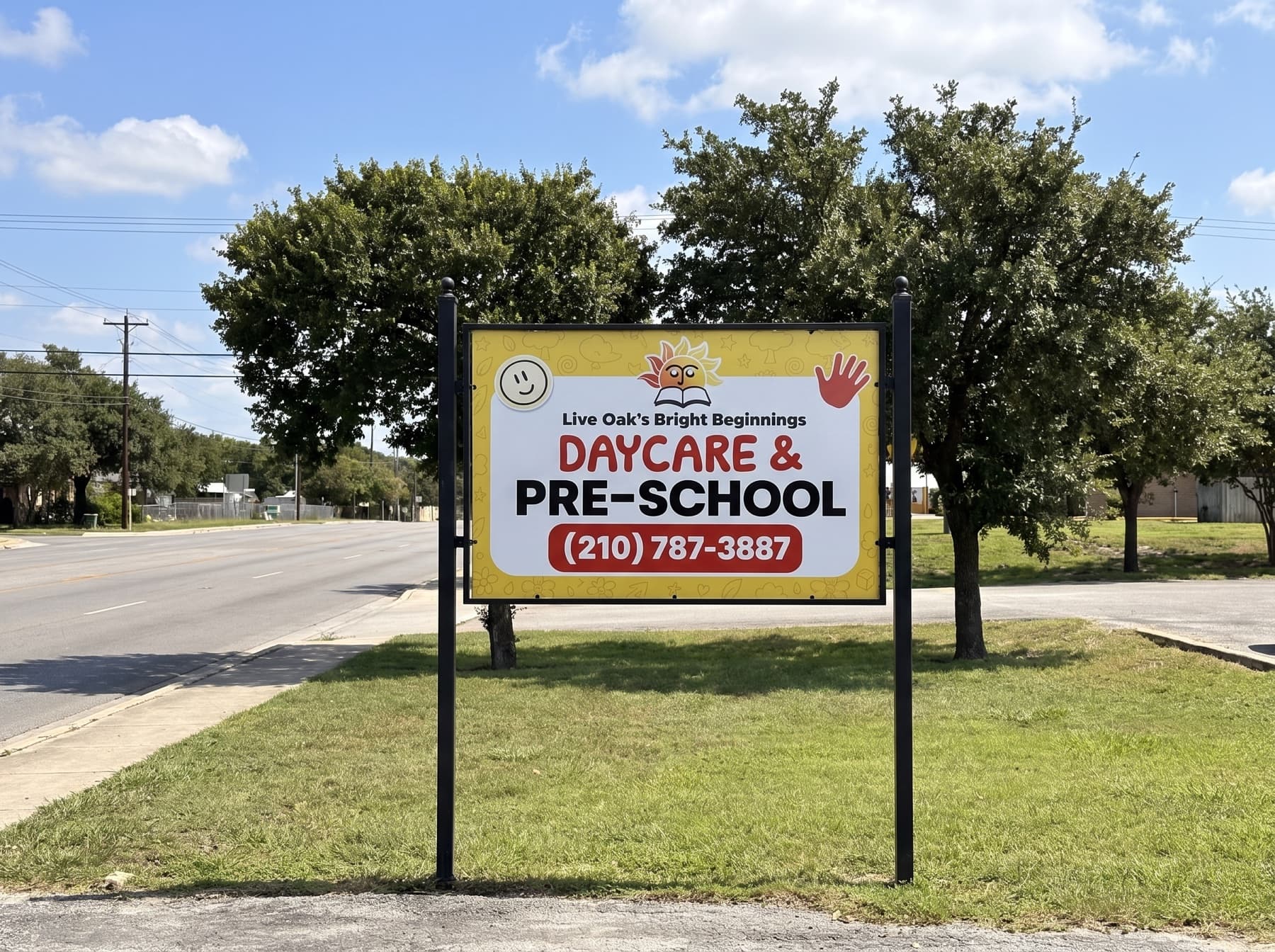 Yellow and white Bright Beginnings Daycare and Pre-School sign on two black posts at the street edge on a sunny day, centered with the road and live oaks behind