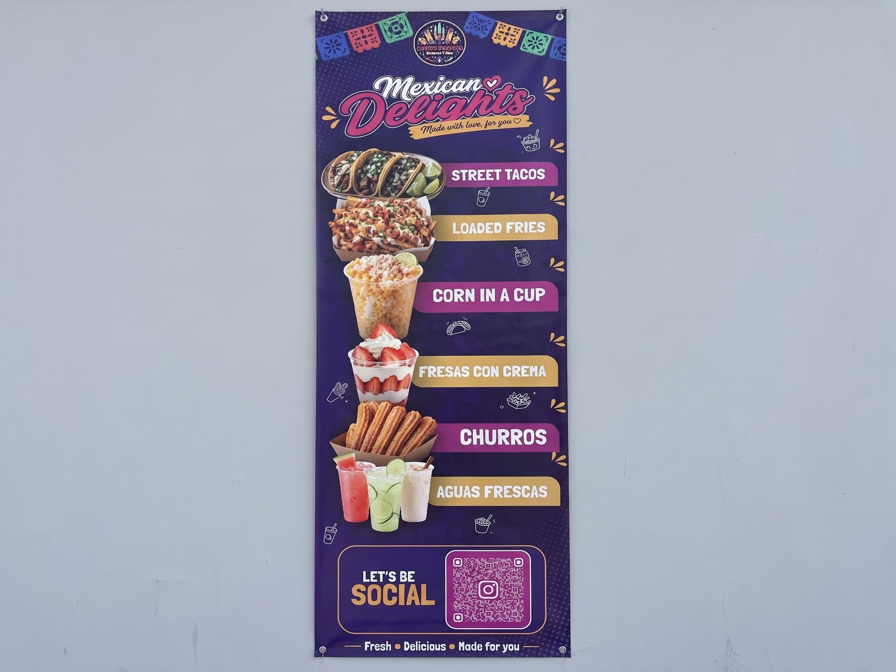 Carito's Snackaria menu banner hanging flat on a wall, every item photographed and labeled down the panel with a scannable social code at the bottom