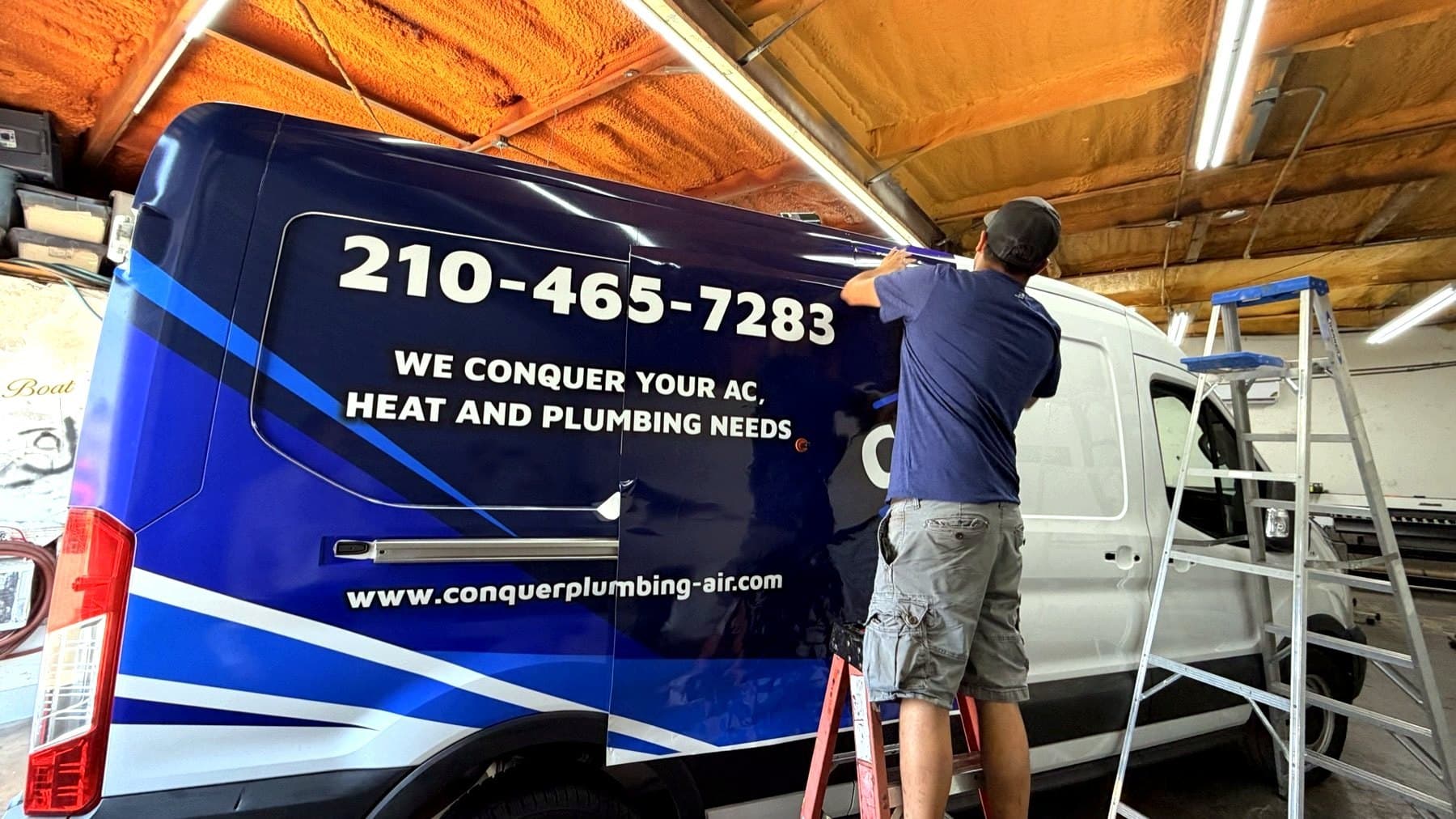 Shop photo of the Conquer Plumbing and Air van wrap going on, taken mid-install