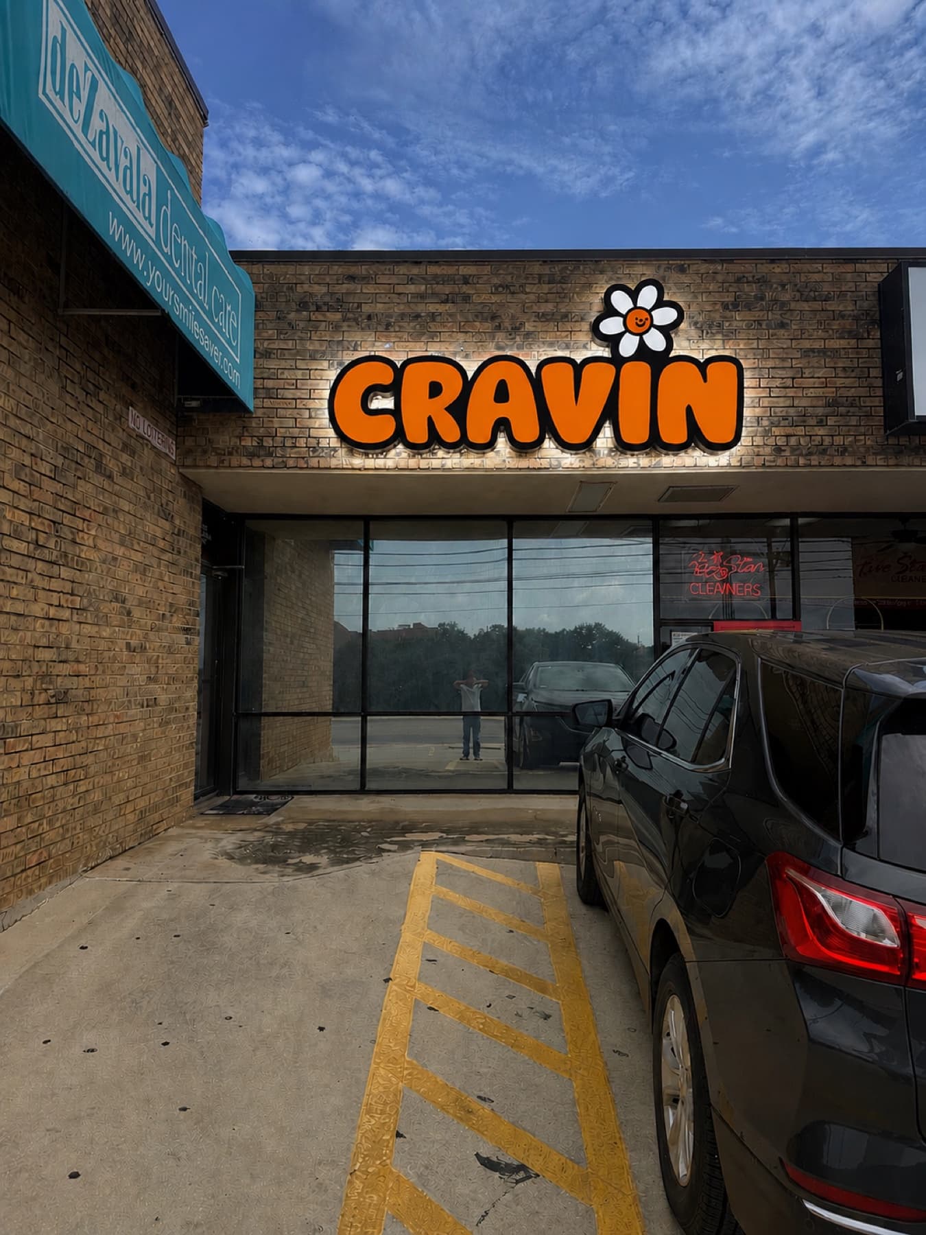 The Cravin sign lit up in the evening, letters and daisy glowing orange against the brick
