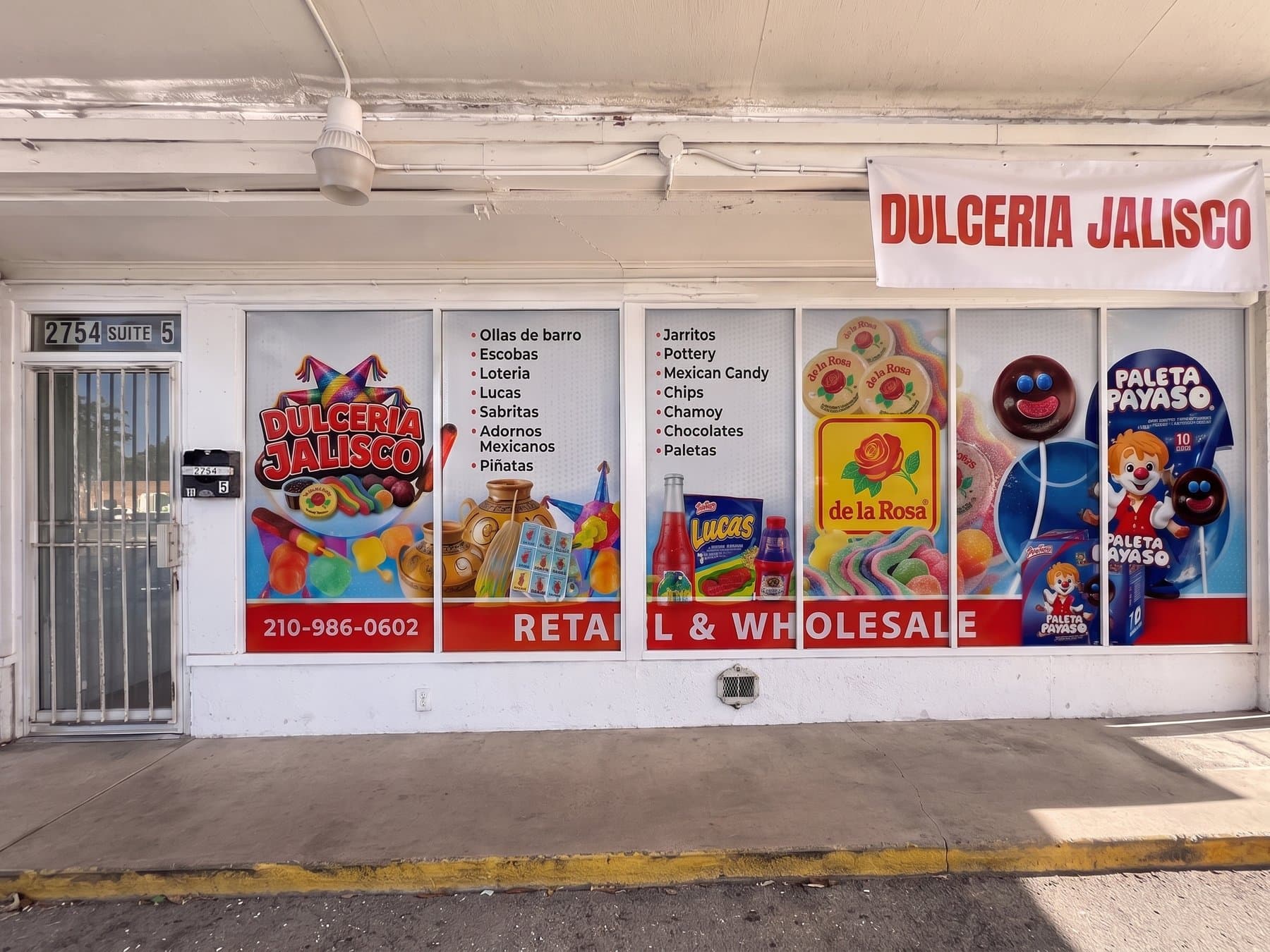 Dulceria Jalisco storefront with printed graphics across six panes, the logo at the left, two columns of what the shop carries, product photography at the right and a red band carrying the phone number, with the name banner hung above the walkway