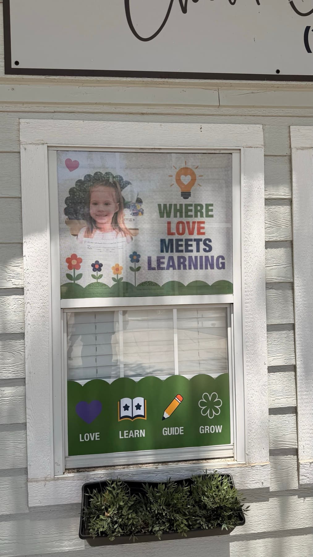 Close view of the Where Love Meets Learning window panel with a child's photo and the green Love Learn Guide Grow band below