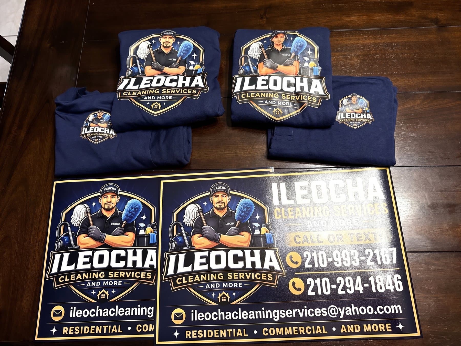 Ileocha Cleaning Services vehicle magnets and folded navy crew shirts laid out together on a wood table before delivery, the same illustrated mark carried on both
