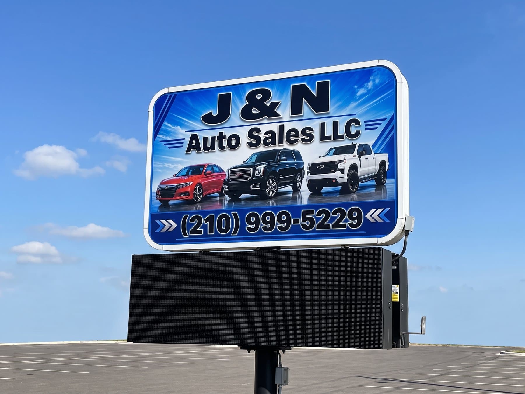 J and N Auto Sales pylon face against a clear sky, three vehicles across the blue field with the phone number in a band underneath, mounted above the lot's LED message board