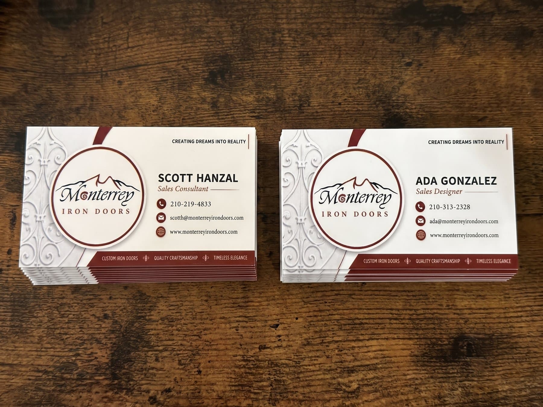 Two stacks of Monterrey Iron Doors business cards on a dark wood table, one set for the sales consultant and one for the sales designer, printed off a single layout
