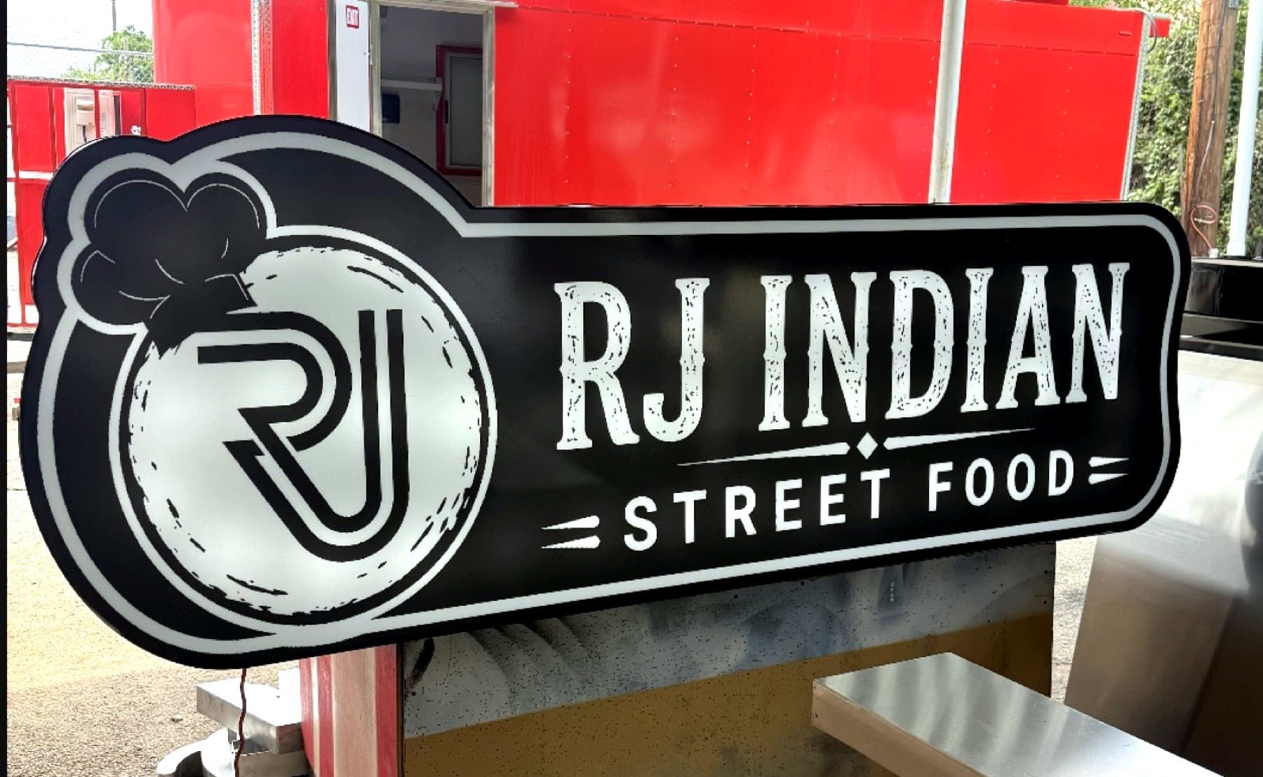 Delivery photo of the RJ Indian Street Food sign propped against the client's trailer before handoff