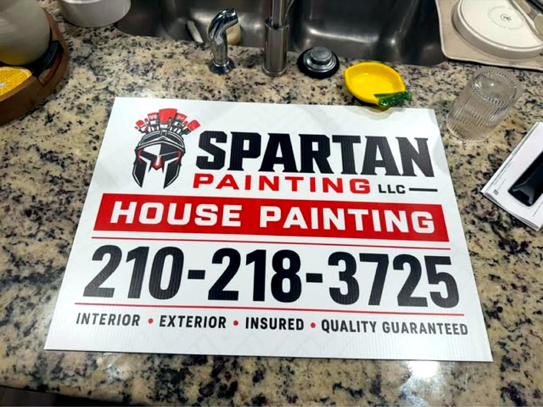 Delivery photo of the Spartan Painting yard sign laid flat indoors before pickup
