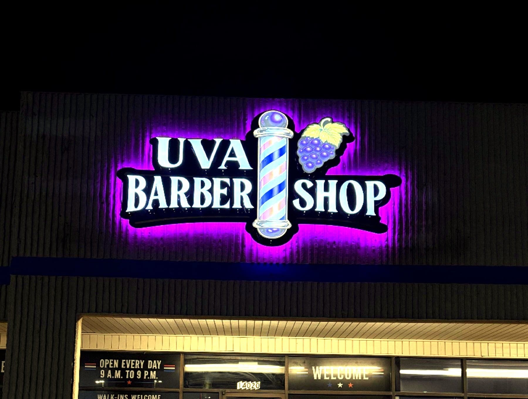 Night photo of the UVA Barber Shop sign lit on the storefront fascia, taken on site
