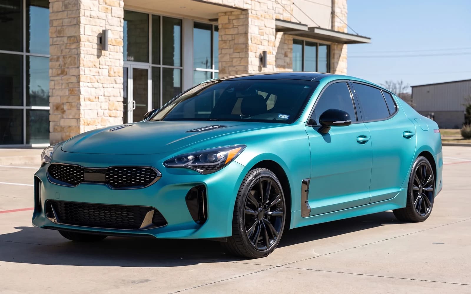 Illustration of a sedan in a solid satin teal color change film with a gloss black roof and mirror caps, and no lettering or graphics