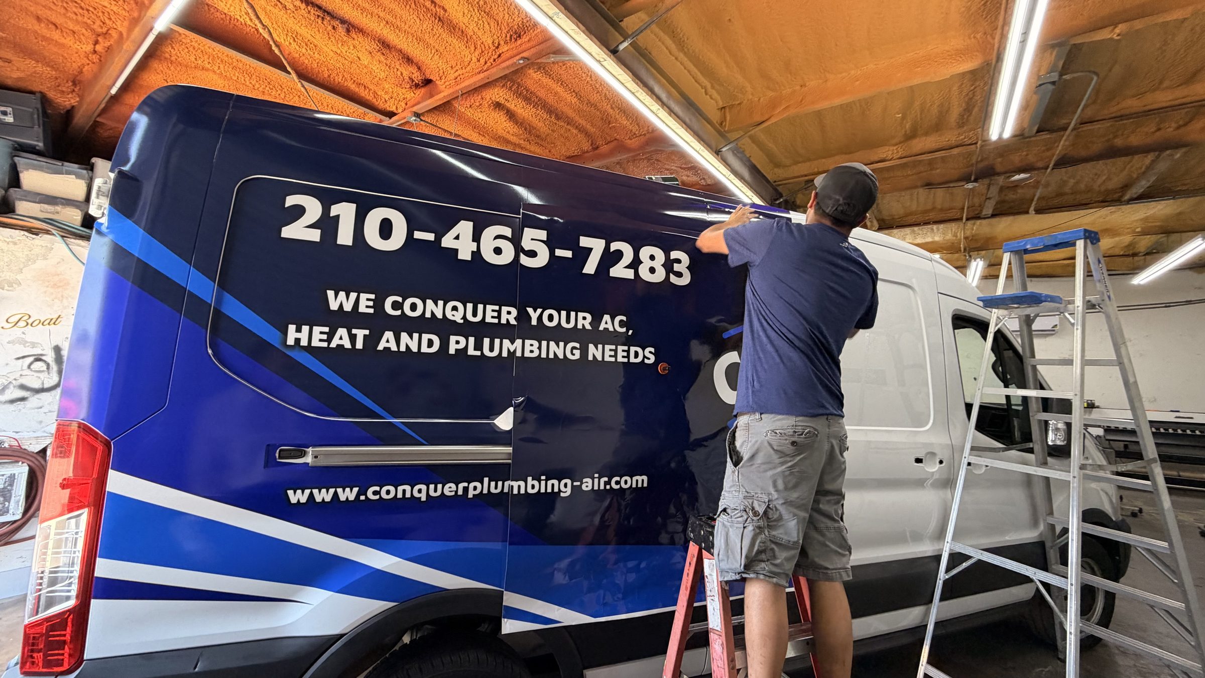 An installer on a ladder applies a vehicle wrap to a white cargo van